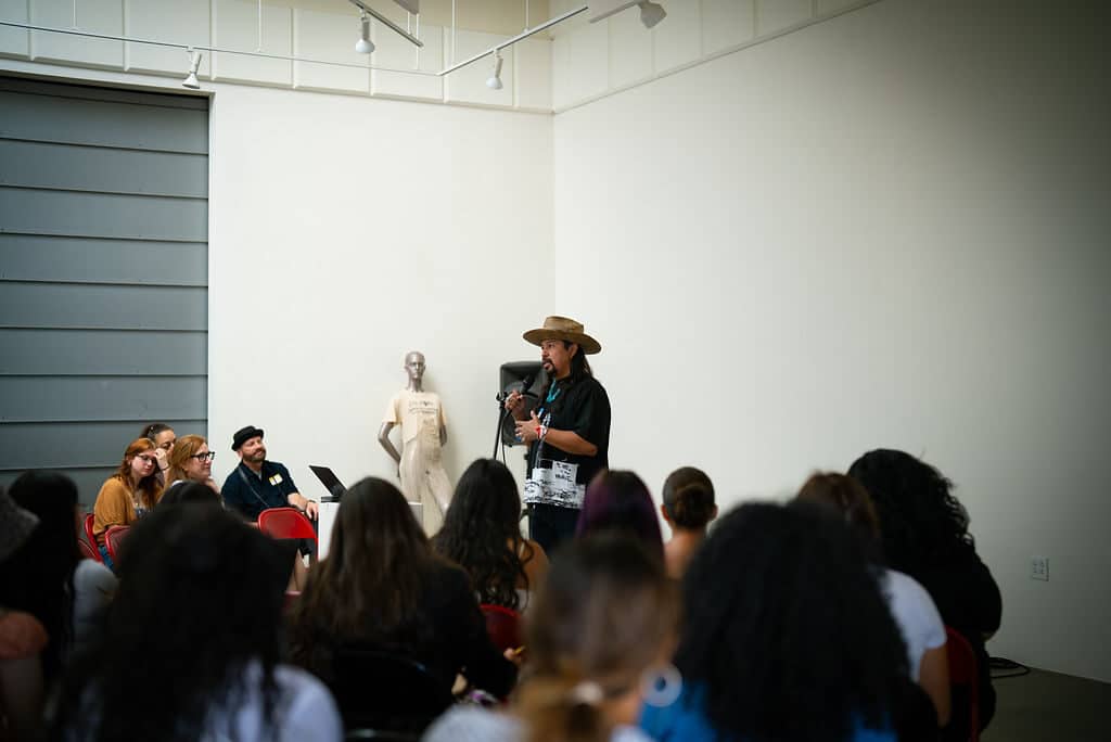 A speaker presents to seated students during Indigenous Fashion 4EVER