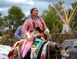 Apsáalooke woman on horseback in pink floral beadwork regalia at the Crow Fair Parade.