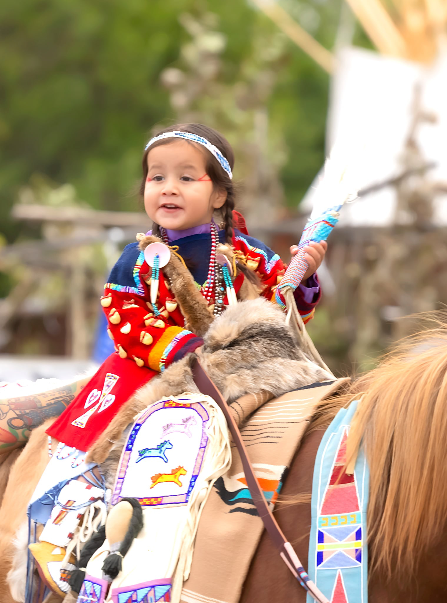 Young Apsáalooke child in red floral beadwork regalia riding in the Crow Fair Parade.