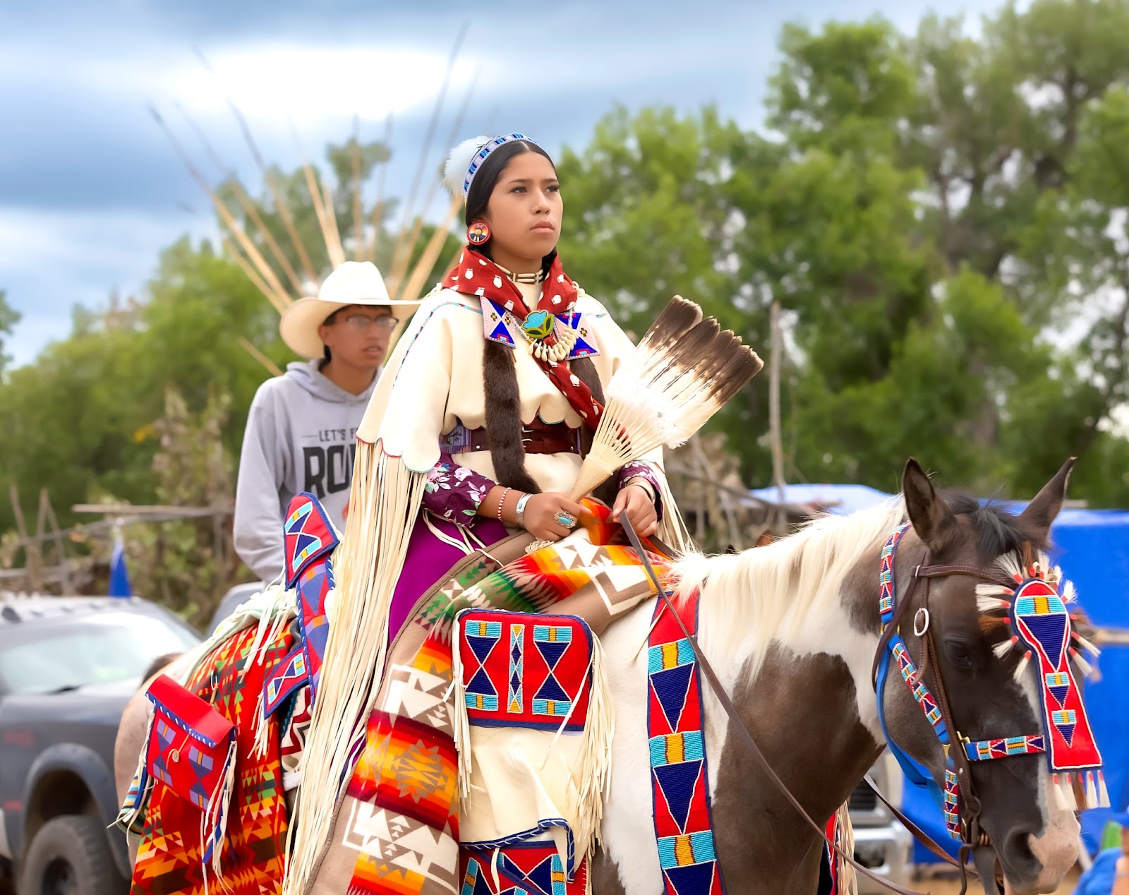 Apsáalooke woman in a cream elk tooth dress and beaded belt riding at Crow Fair.
