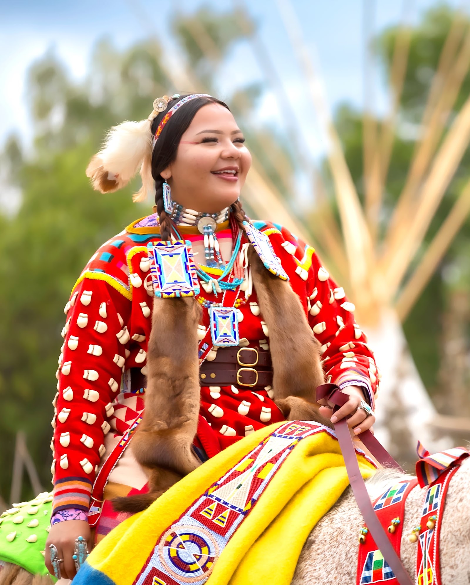 Smiling Apsáalooke woman in red regalia with beaded necklace at the Crow Fair Parade.