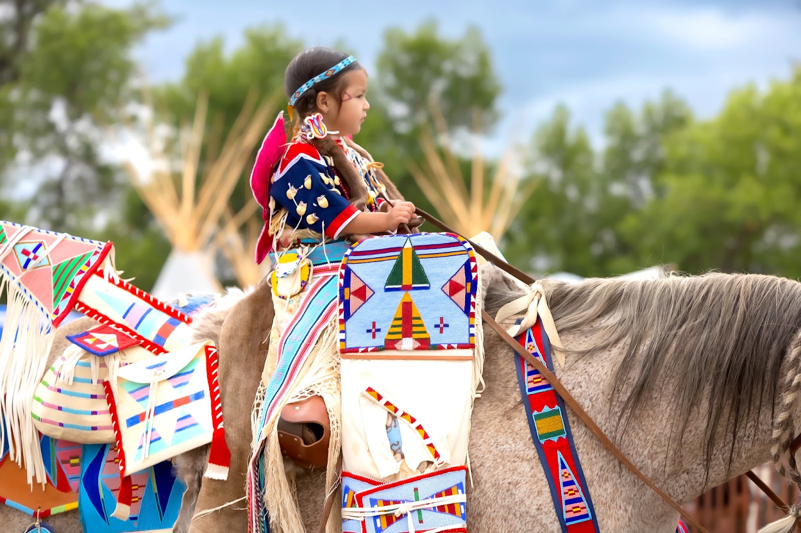 Young rider with a large blue and white beaded martingale on horseback at Crow Fair.