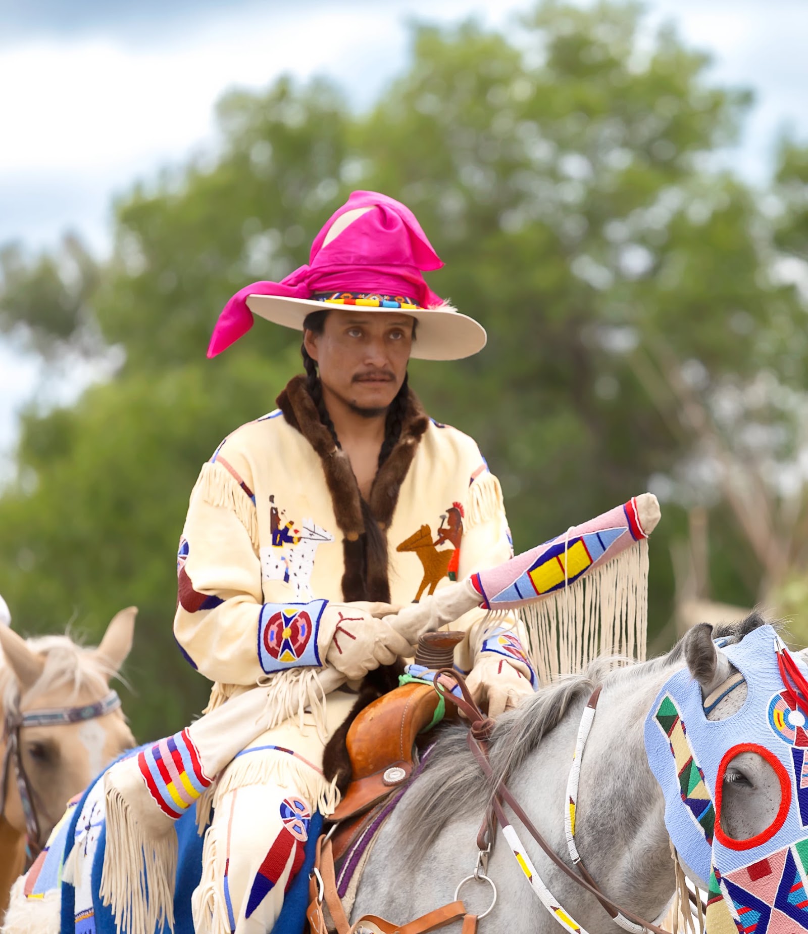 Man in a pink cowboy hat and beaded regalia riding in the Crow Fair Parade.